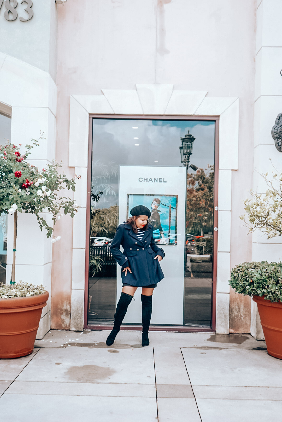 Chanel storefront add with a woman in navy coat, black beret, striped shirt, and over the knee black suede boots.