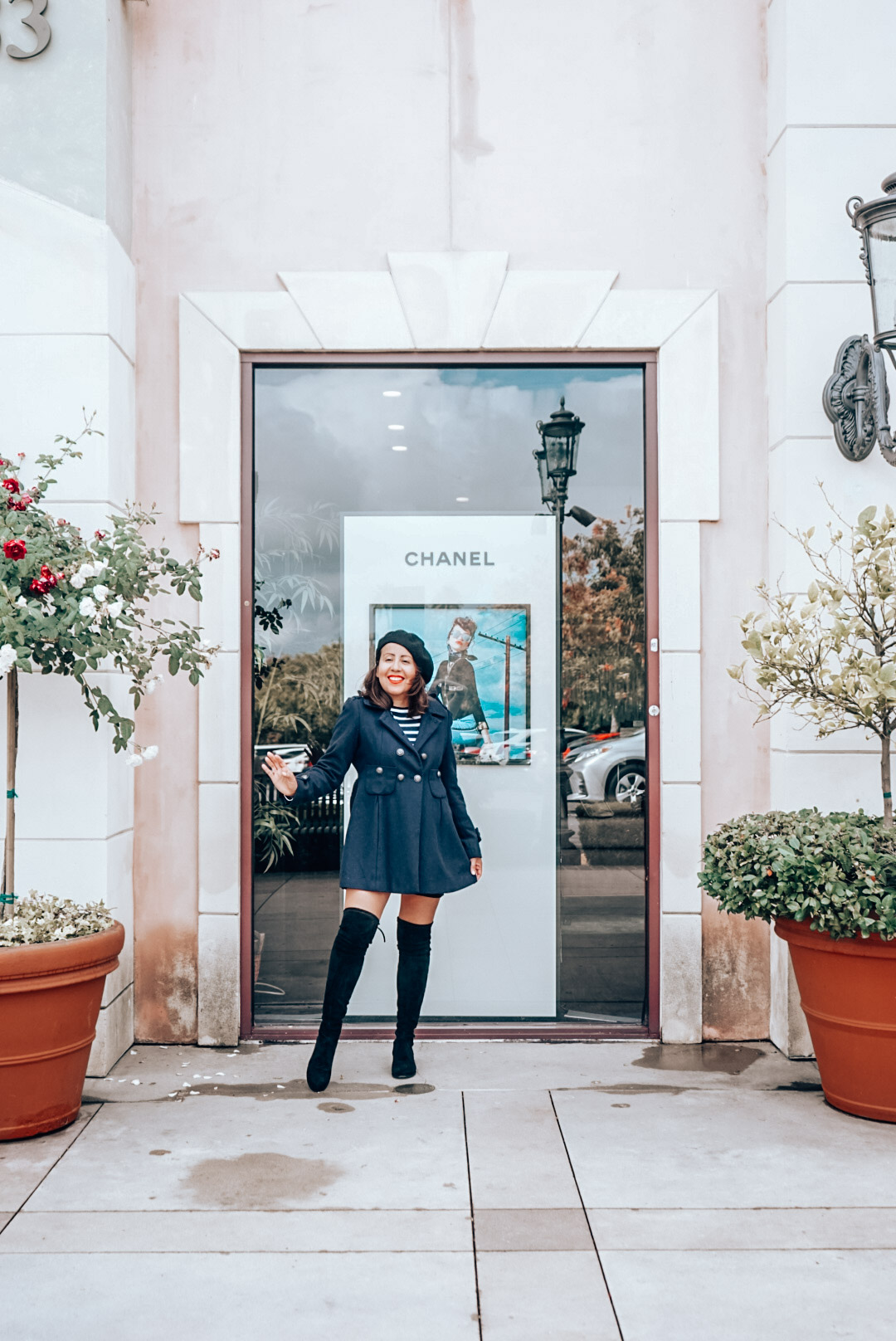 Chanel storefront add with a woman in navy coat, black beret, striped shirt, and over the knee black suede boots.