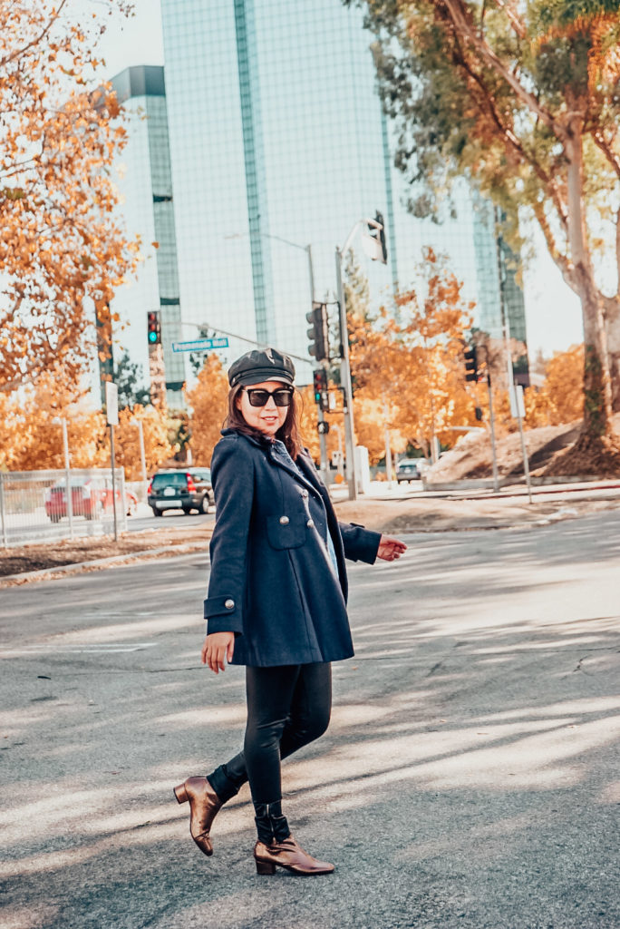 Autumn foliage, and girl in navy peacoat and ankle boots wearing a newsboy hat.