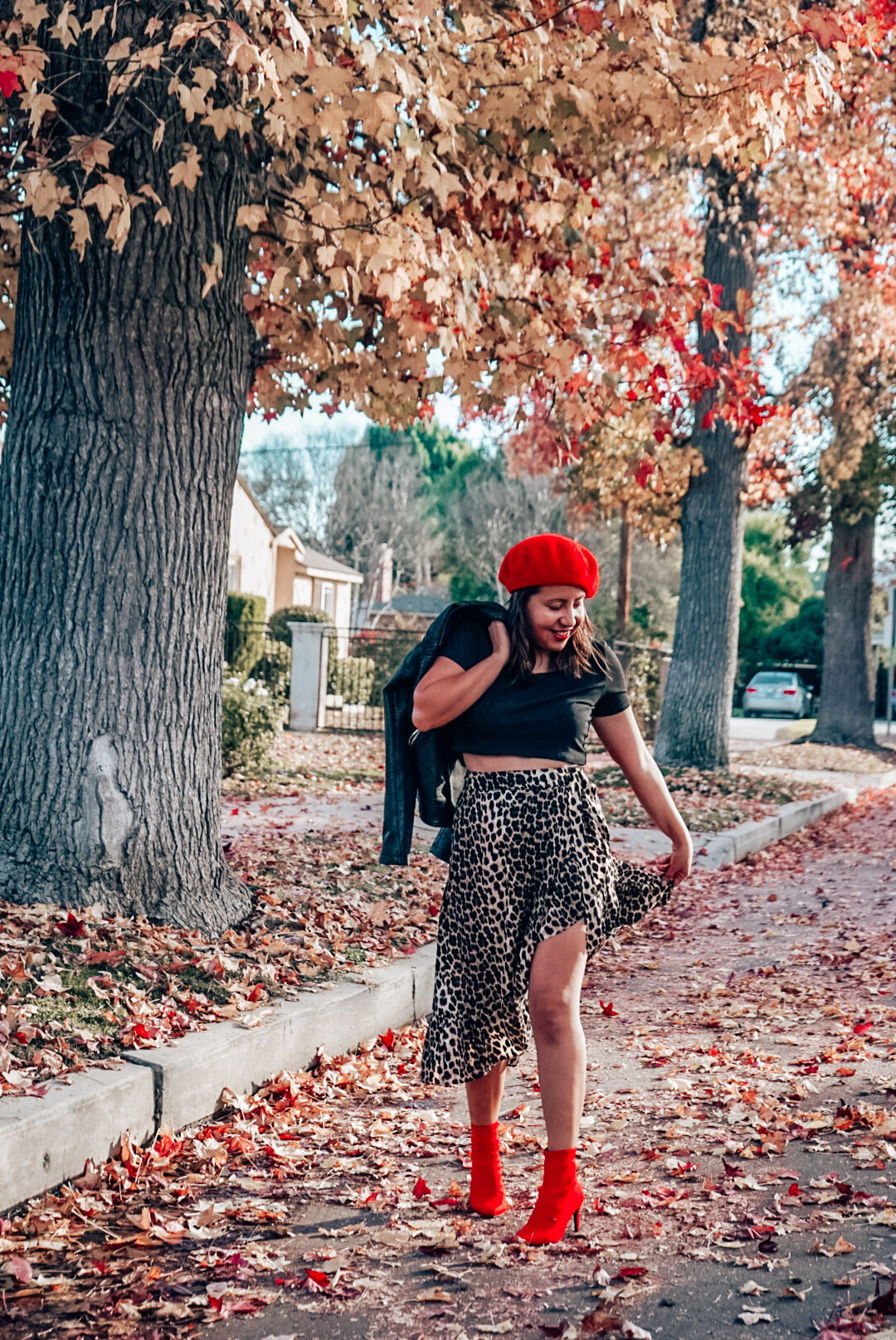 A woman wearing leopard print midi skirt and faux leather jacket with red beret and red ankle boots smiling.