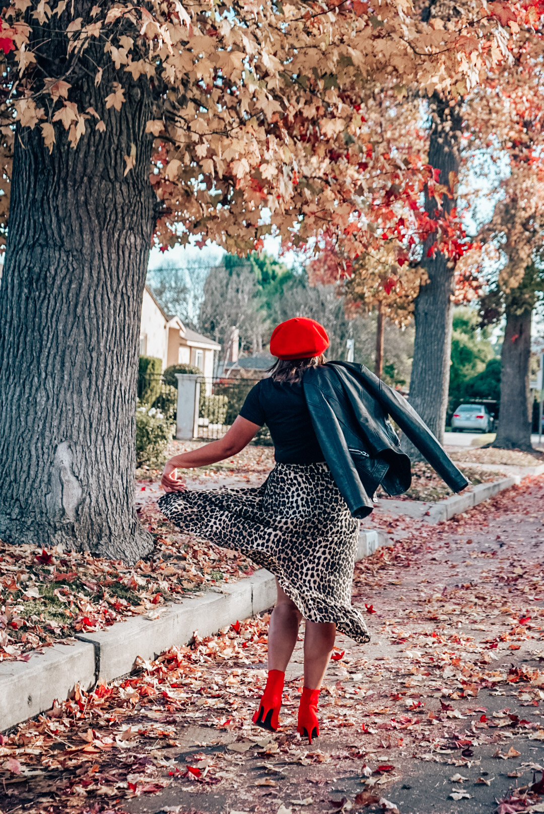 A woman wearing leopard print midi skirt and faux leather jacket with red beret and red ankle boots twirling.