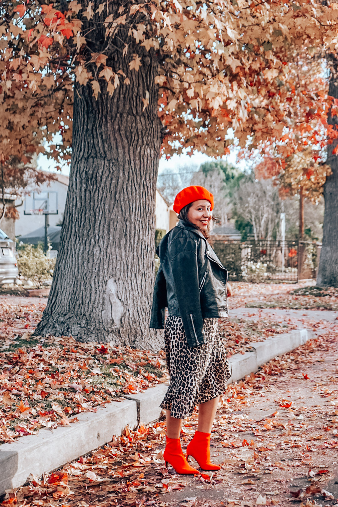 A woman wearing leopard print midi skirt and faux leather jacket with red beret and red ankle boots smiling.