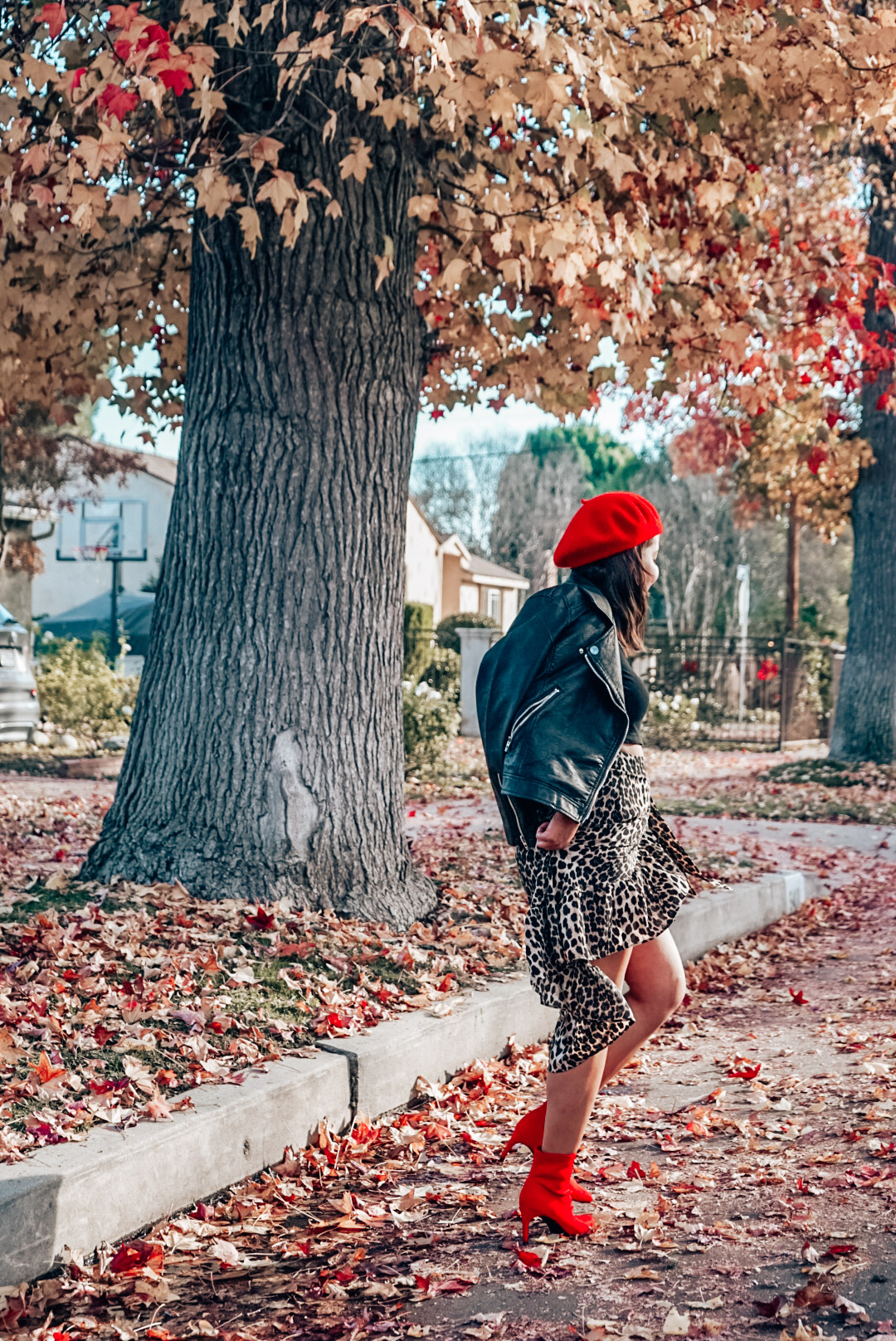 A woman wearing leopard print midi skirt and red beret walking away.