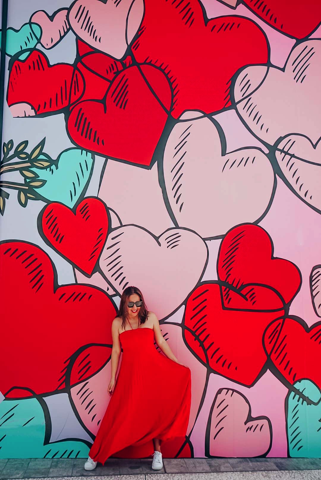 Girl in long red maxi dress against a heart mural.