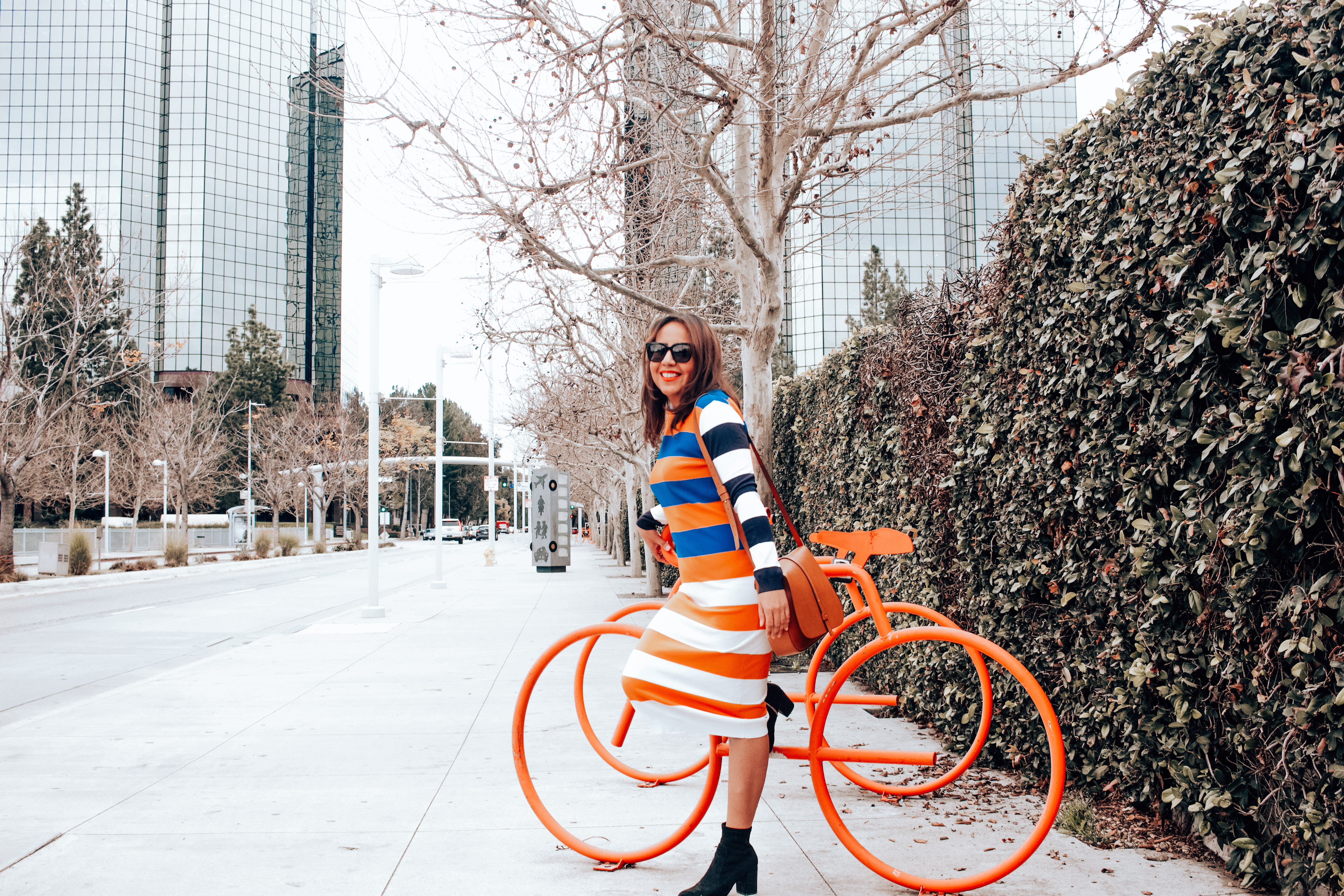 Girl in striped sweater dress in the city next to bikes. 
