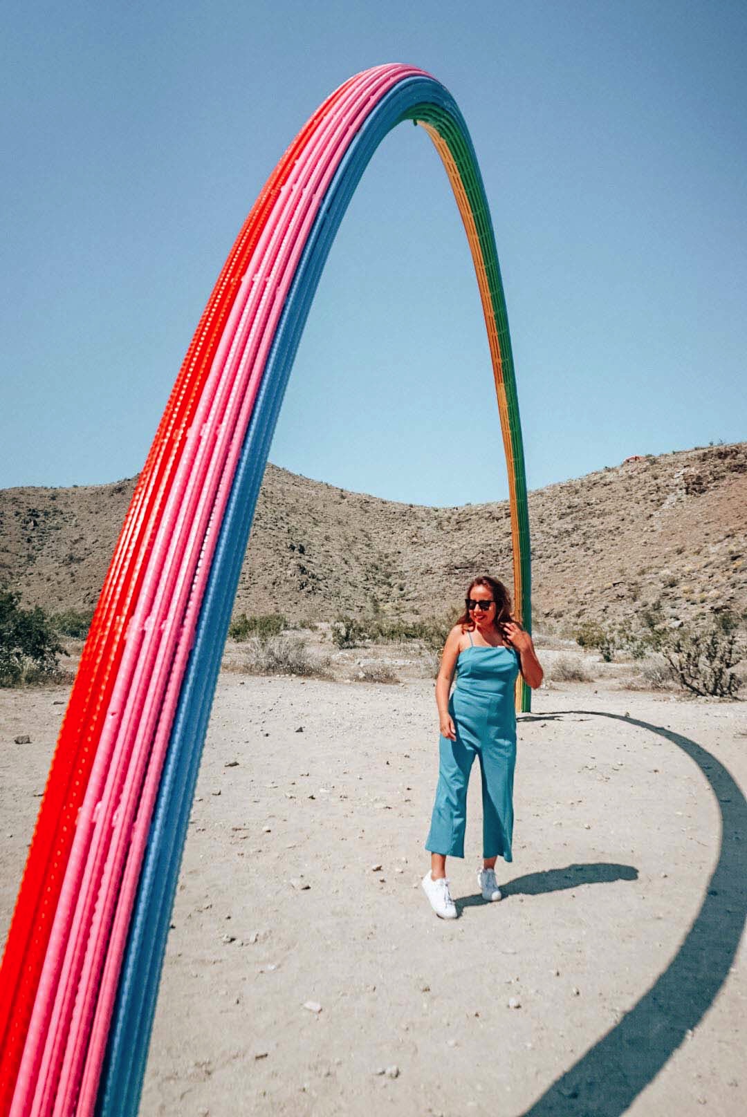 Girl wearing blue jumpsuit under the Lover's Rainbow sculpture in Rancho Mirage. Sculpture is part of the Superflex in the Coachella Valley. 