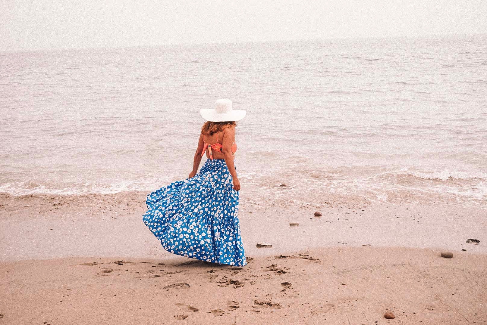 Woman in long tiered blue floral printed skirt at the beach. 