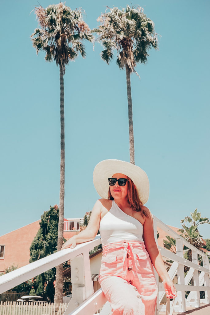 Girl in Los Angeles wearing one shoulder top and button front midi skirt standing in front of palm trees.